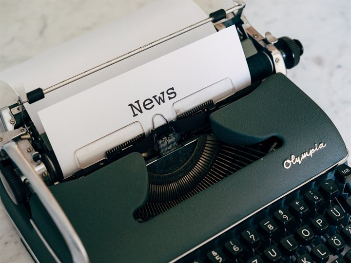 Ouderwetse typemachine met wit blaadje waarop in het Engels 'news' staat geschreven.